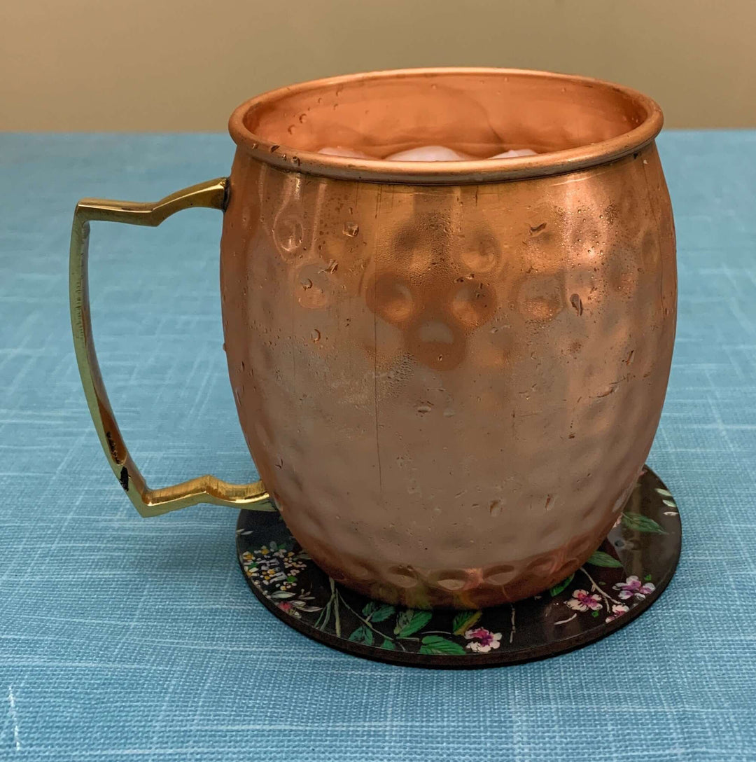 Handcrafted Hammered Copper Moscow Mule Mugs (Set of 4), chilled drinkware on a floral coaster.