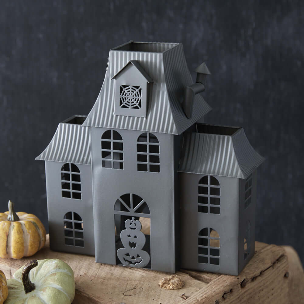 Haunted House Halloween metal tealight luminary with pumpkins, featuring arched windows and weathered finish for nostalgic decoration.