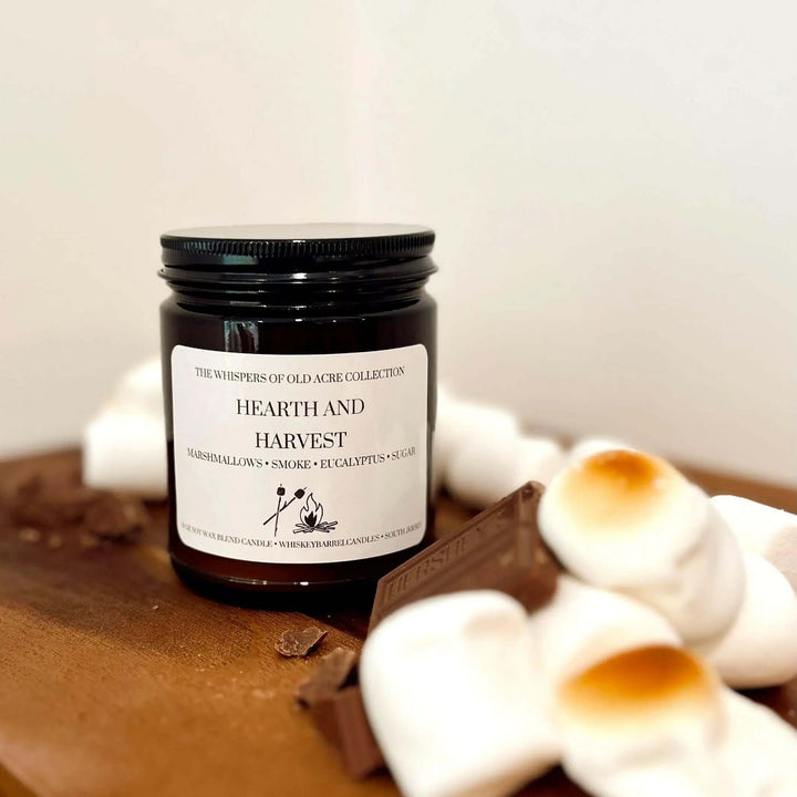 Hearth and Harvest Scented Candle: Marshmallow, Smoke & Eucalyptus with marshmallows and chocolate on a wooden board.
