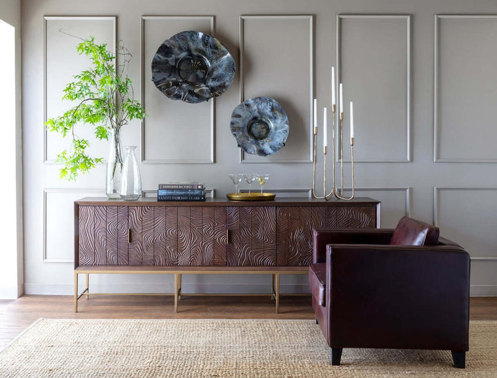 Modern living room with wooden console, glass vases, contemporary art, leather chair, and a stylish candelabra.