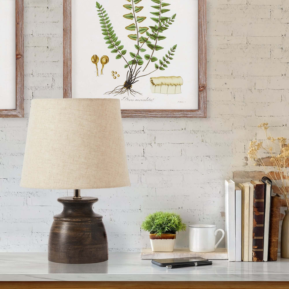 Petite mango wood desk lamp with natural linen shade in a cozy home setting, surrounded by plants and books.