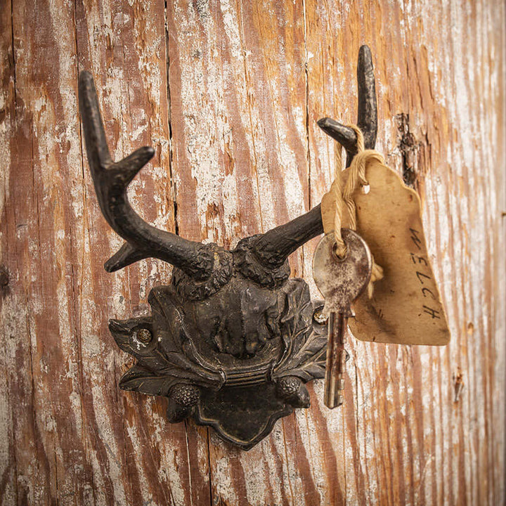 Vintage rustic antler wall hook with key, showcasing lodge-inspired design and natural wood background.