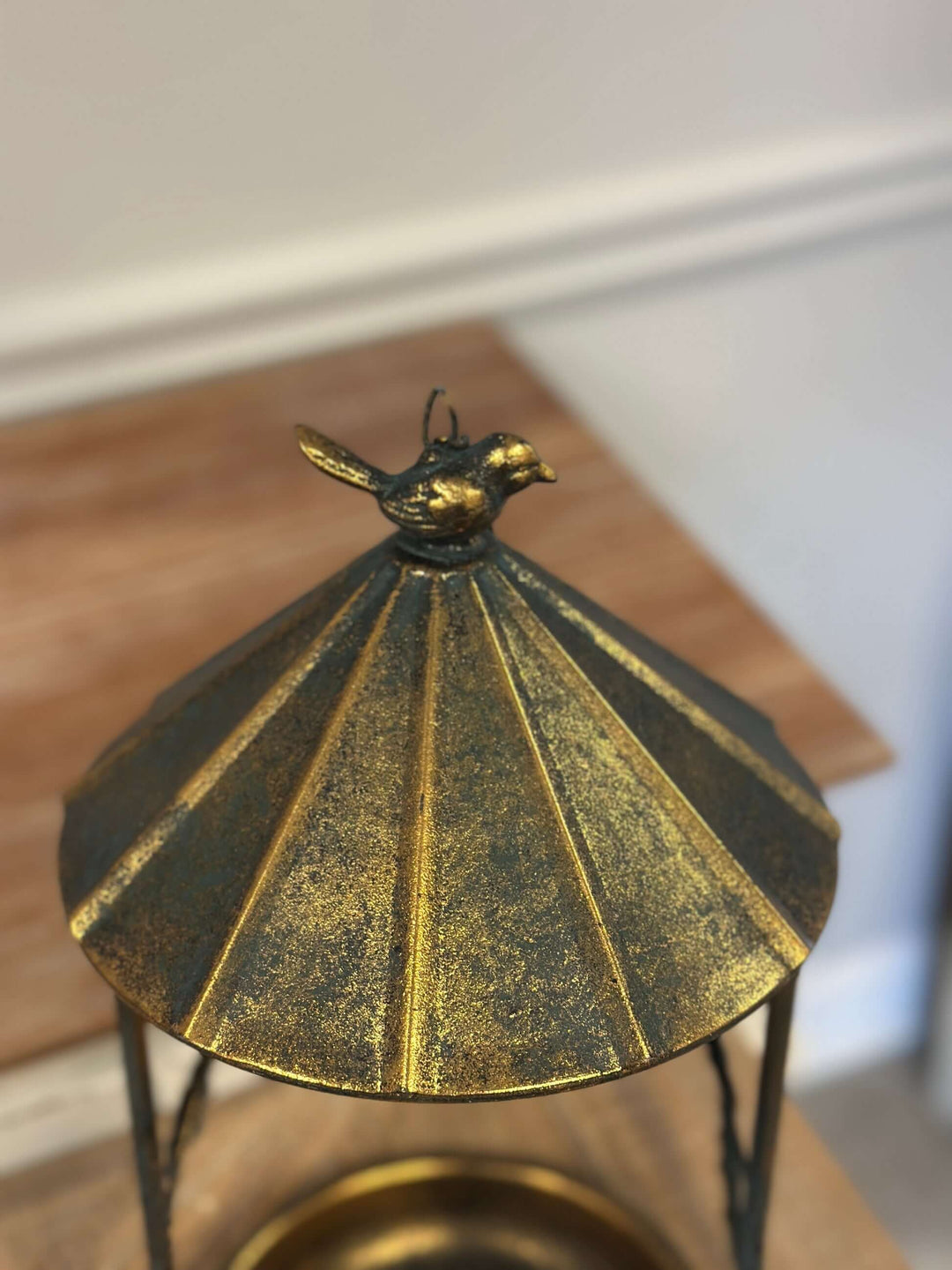 Rustic bronze hanging bird feeder featuring a leaf and bird design with a sloped roof mimicking an antique gazebo.
