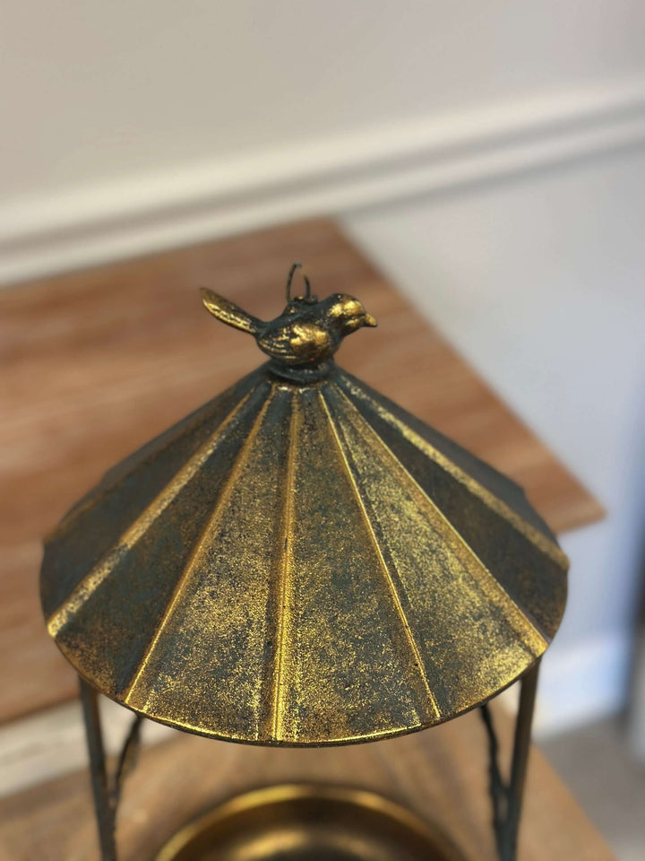 Rustic bronze hanging bird feeder featuring a leaf and bird design with a sloped roof mimicking an antique gazebo.
