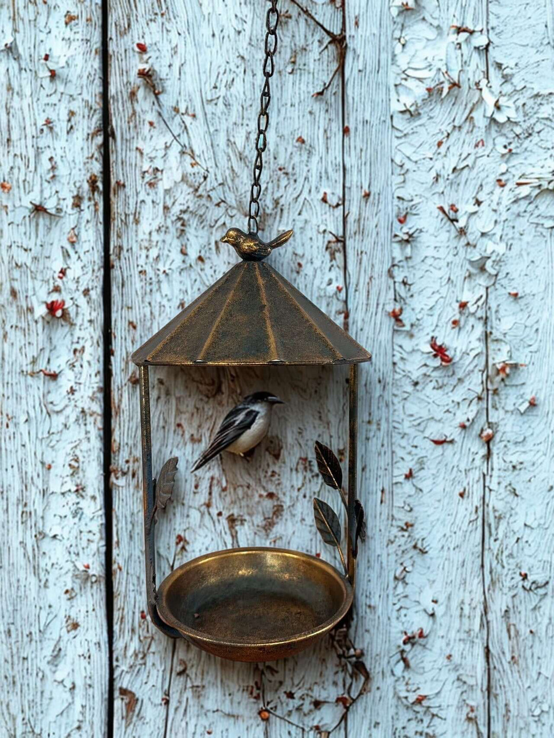 Rustic bronze hanging bird feeder with leaf and bird design against a weathered wood backdrop