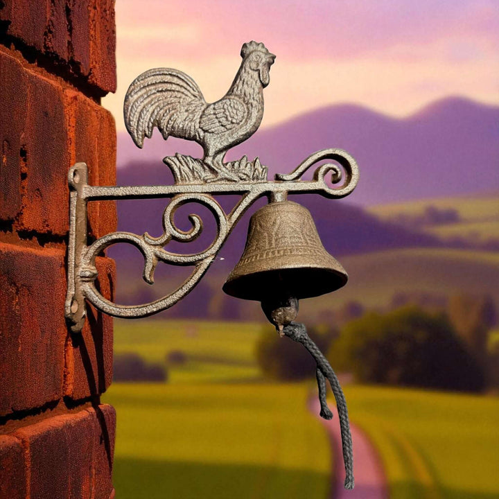 Rustic Cast Iron Farmhouse Rooster Wall Bell mounted on brick wall with countryside backdrop.