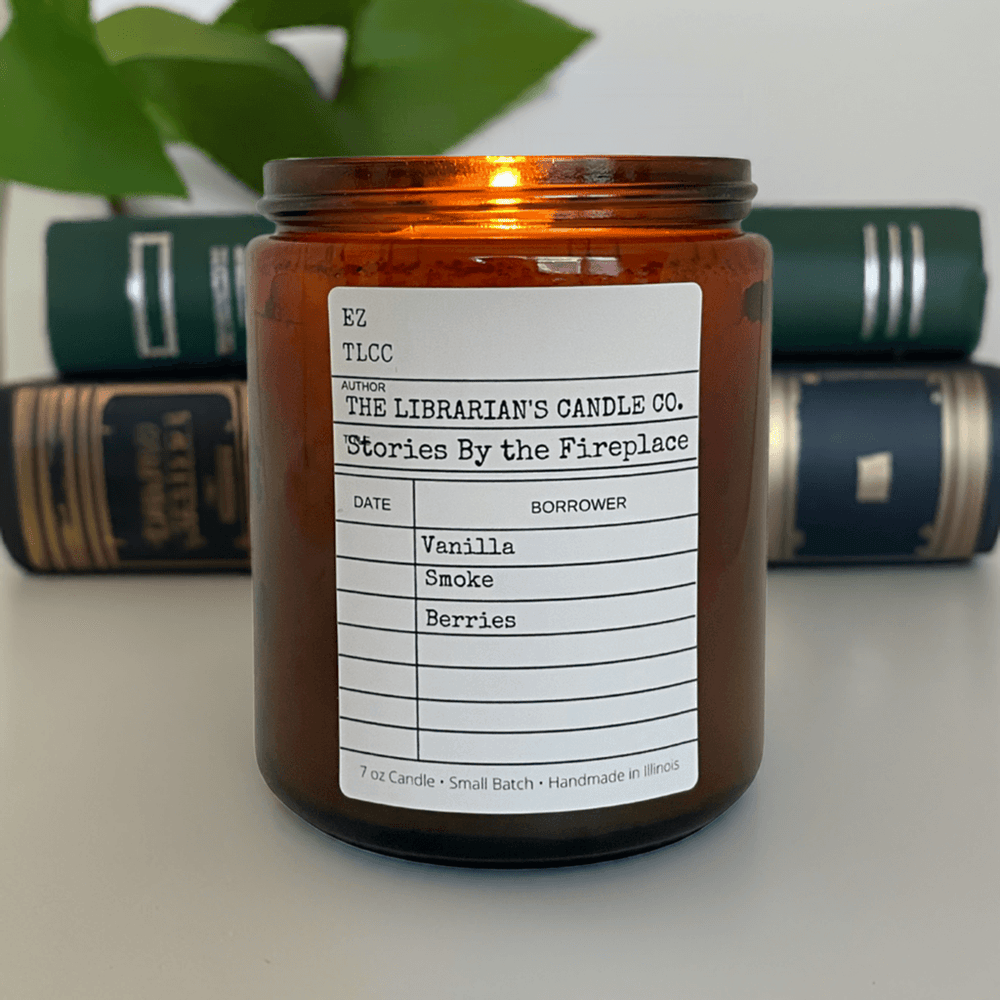 Stories by the Fireplace Candle: Smoked Vanilla & Berries, amber jar, with books in the background, infused with vanilla, smoke, and berries scent.
