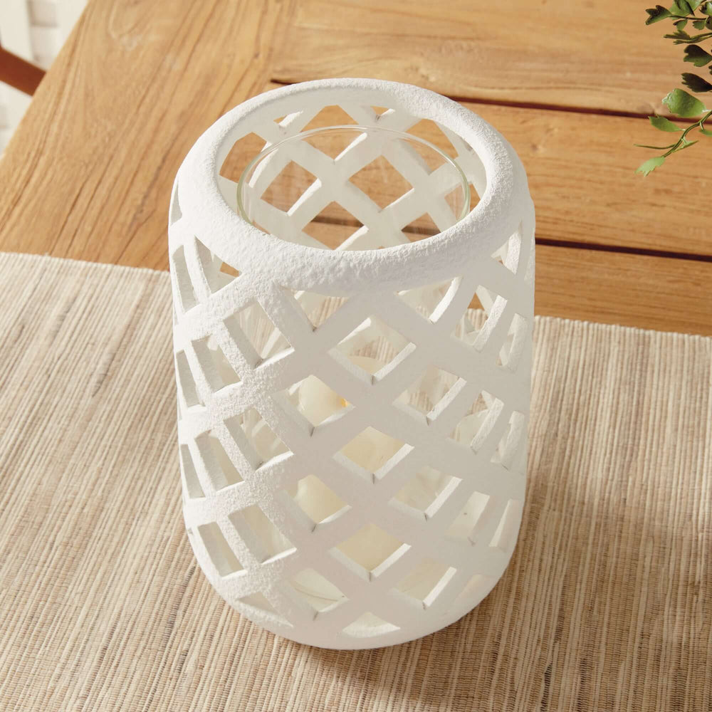 Terracotta hurricane candle holder with glass insert showcasing an airy lattice design on a wooden table.