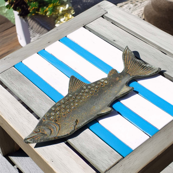 Vintage cast iron fish-shaped tray with rustic patina on a blue and white striped table outdoors.