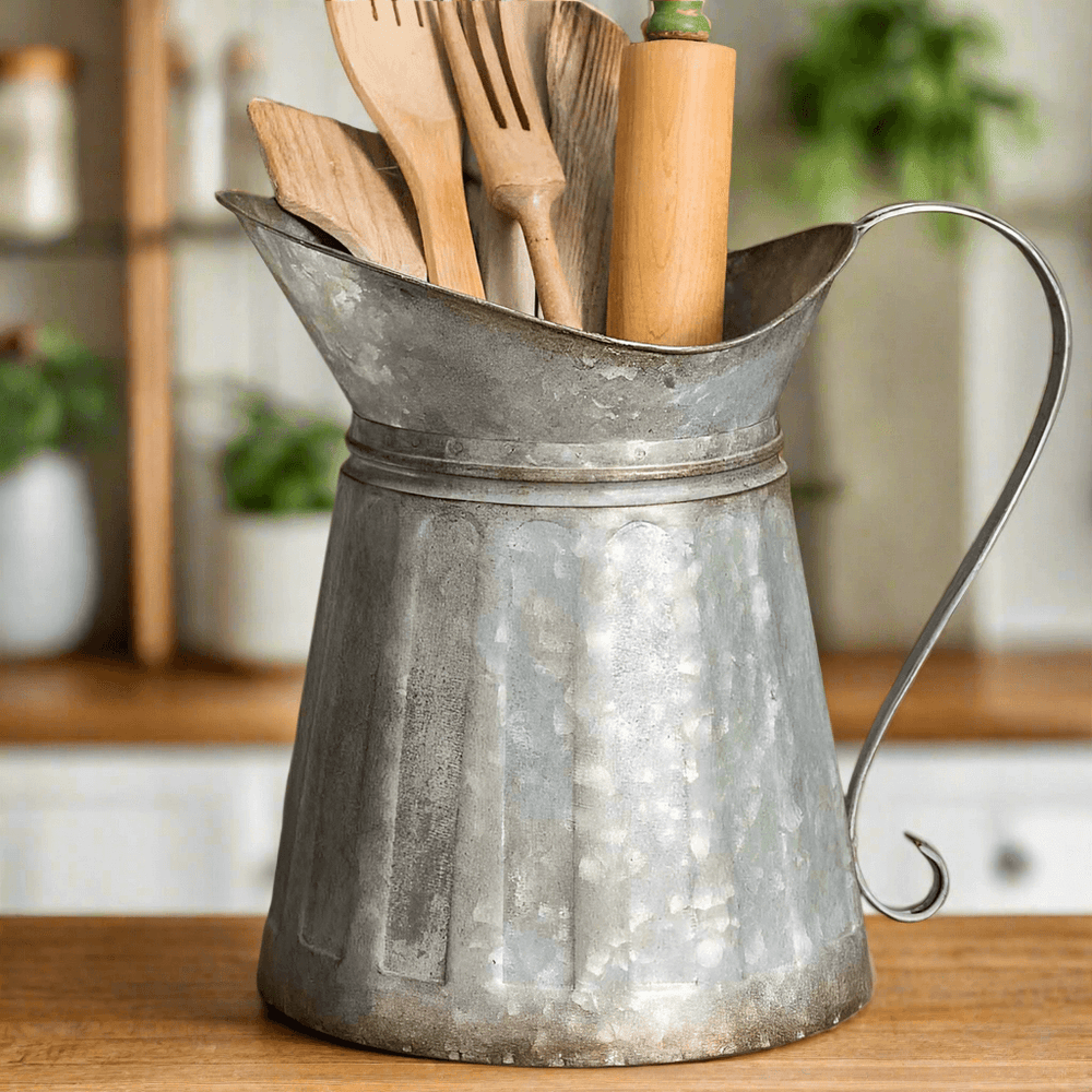 Vintage galvanized metal pitcher utensil holder with wooden cooking tools, showcasing rustic farmhouse charm.