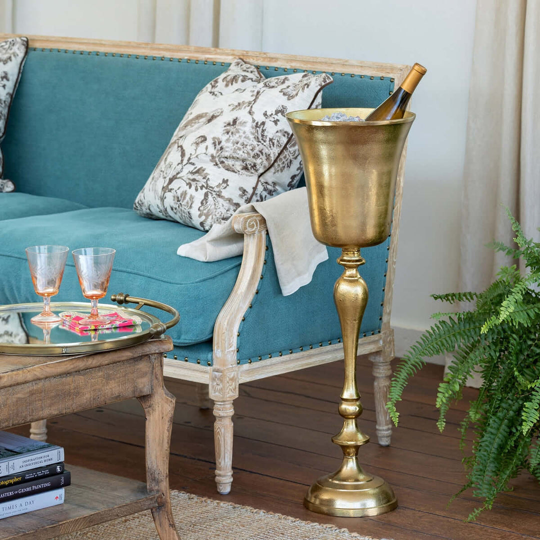 Vintage gold cast aluminum wine chiller with sculptural design, ideal for elegant gatherings, displayed beside a sofa and glass table.