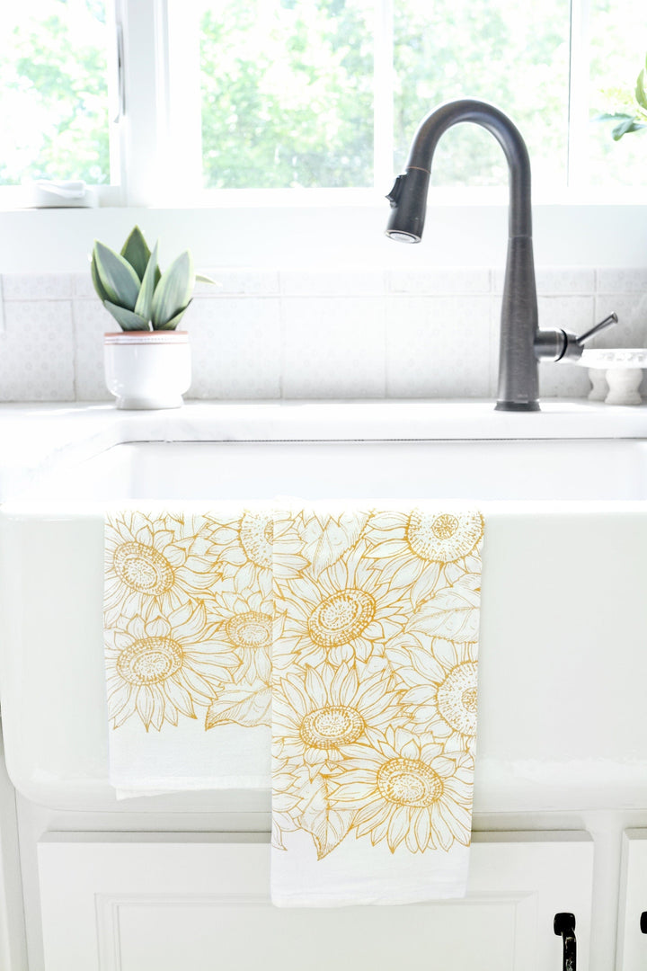 Vintage Sunflower Tea Towel with golden sunflower design hanging by a kitchen sink, adding a rustic touch to the decor.
