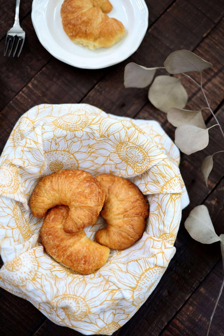 Croissants on a Vintage Sunflower Tea Towel in a basket, with a rustic wooden table setting.
