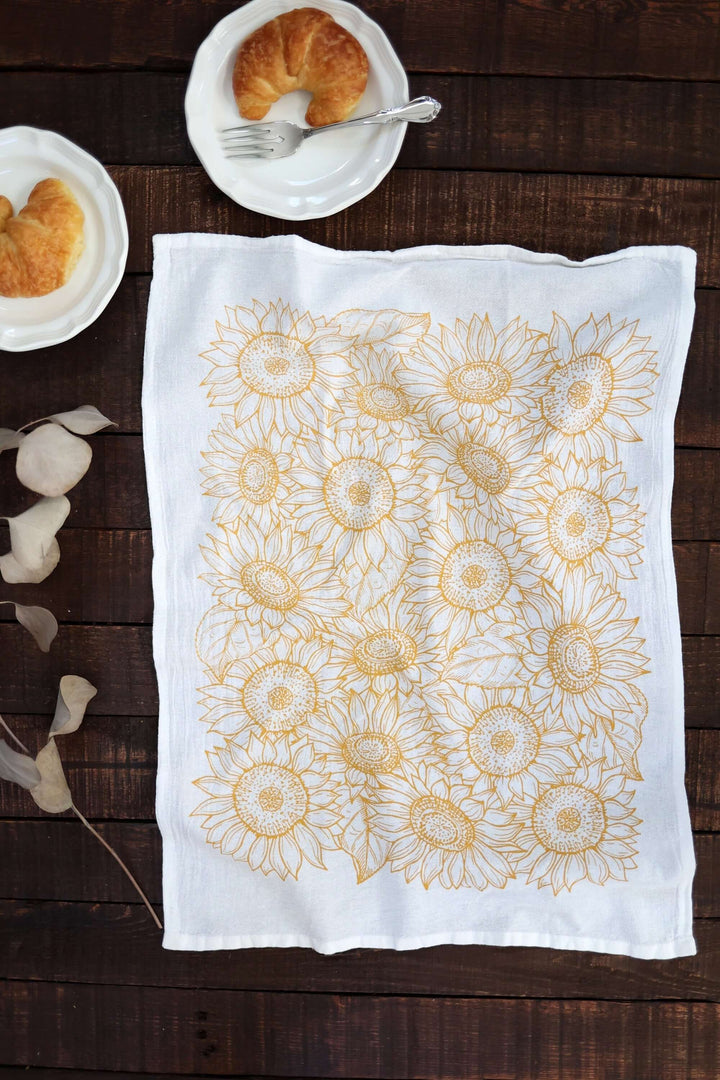 Vintage Sunflower Tea Towel with golden watercolor sunflower design on lint-free cotton, placed on a wooden table with breakfast setting.