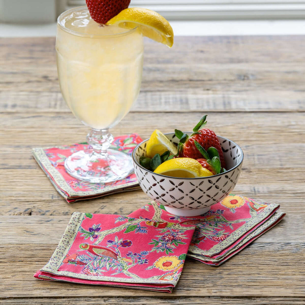 Refreshing drink with fruits on Vintage-Inspired Bird Coral Cotton Cocktail Napkins (Set of 6) on a rustic table.