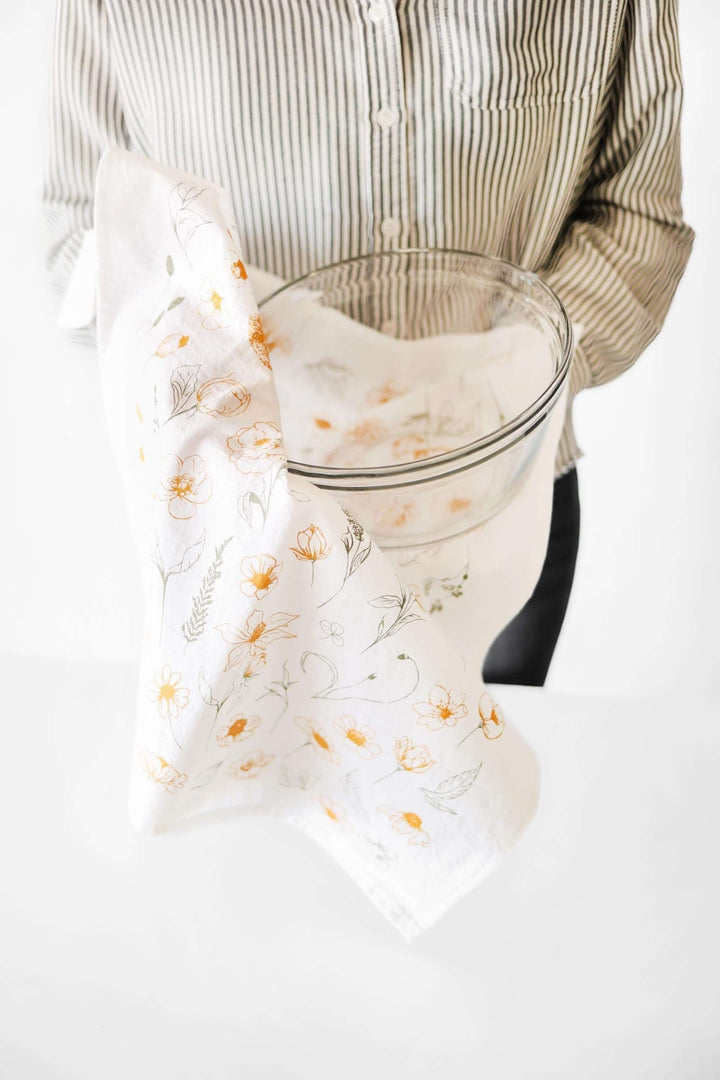 Person holding clear bowl wrapped in Vintage Botanical Flower Garden Tea Towel with golden floral print.