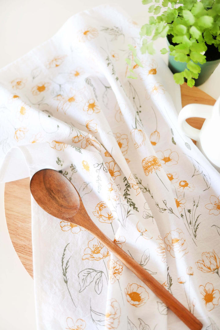 Vintage Botanical Flower Garden Tea Towel with golden blooms and green leaves, draped next to a wooden spoon, enhancing kitchen decor.