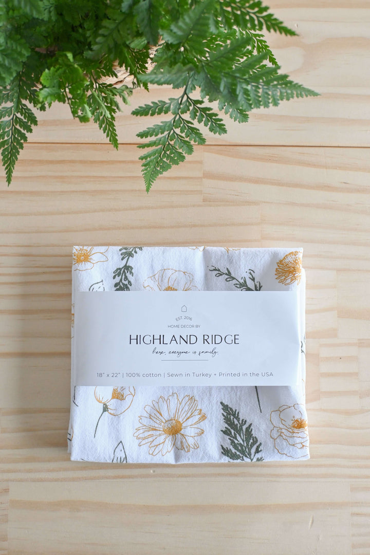 Vintage Botanical Flower Garden Tea Towel with floral print on a wooden table, fern leaves nearby.