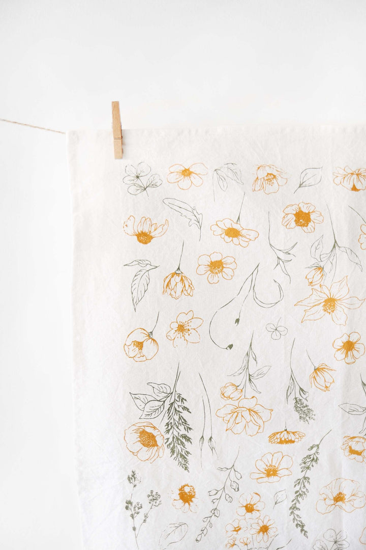 Vintage Botanical Flower Garden Tea Towel with watercolor-style blossoms in golden and green tones hanging on a line.