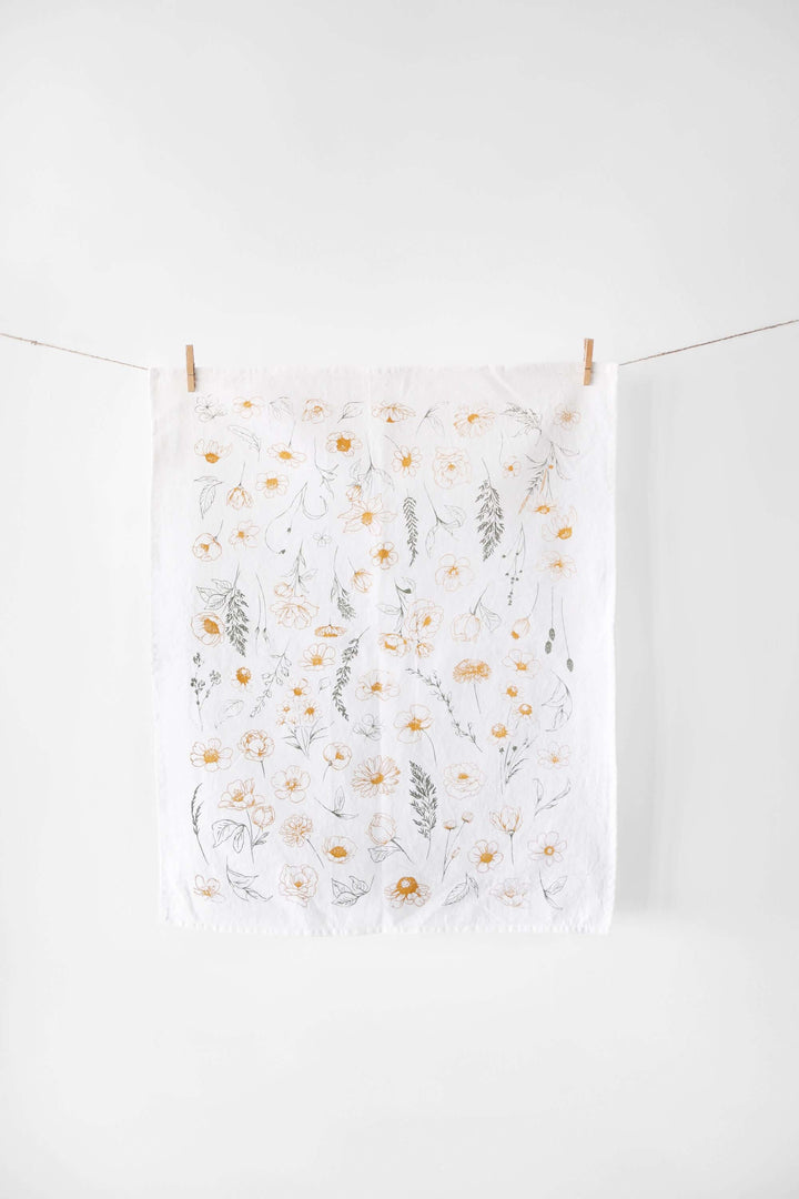 Vintage Botanical Flower Garden Tea Towel with watercolor-style blossoms in warm golden and green tones, hung on display.