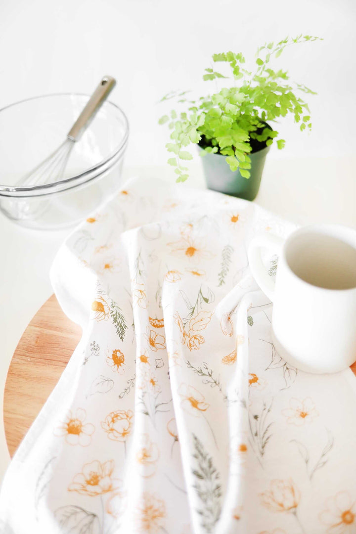 Vintage Botanical Flower Garden Tea Towel with watercolor floral print next to whisk, glass bowl, plant, and mug in a bright kitchen.