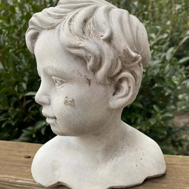Vintage cement boy bust garden statue with detailed curls and serene expression on wooden ledge.