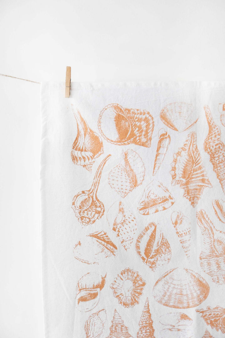 Vintage Coastal Seashell Tea Towel hung, featuring watercolor-style seashell prints evoking a serene seaside ambiance in orange hues.