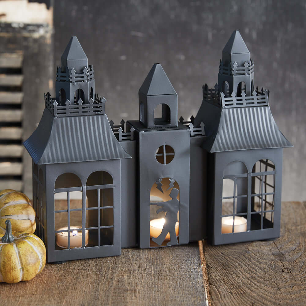 Vintage Frankenstein Castle Halloween metal tealight luminary with gothic design and spires, glowing on a rustic wooden table.