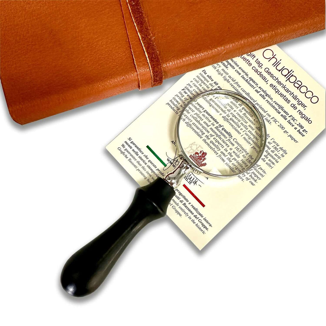 Vintage Handheld Magnifier with Wood Handle resting on a document beside a leather-bound book.