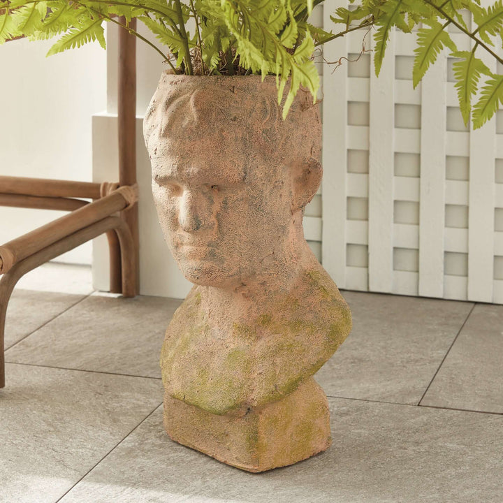 Vintage moss terracotta male bust planter exuding classical elegance and ancient Roman charm, surrounded by greenery.