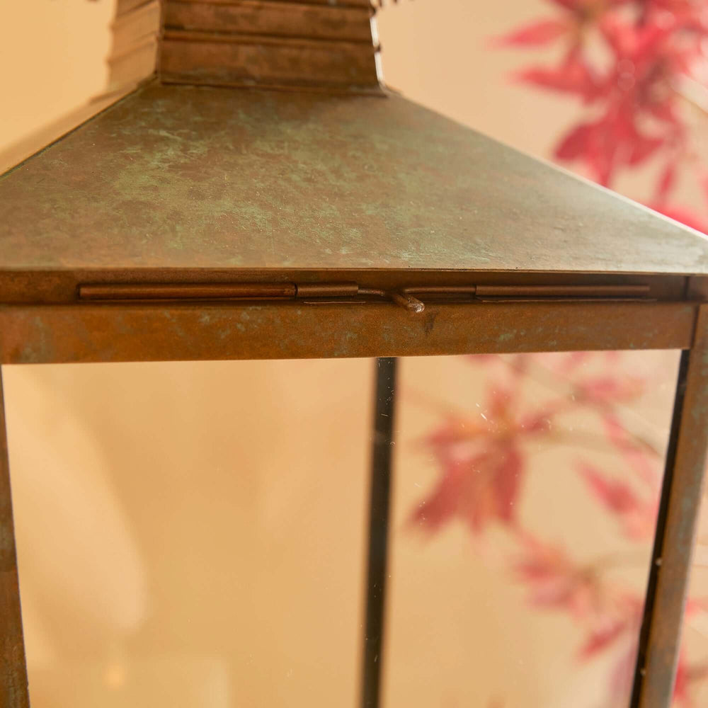 Vintage pagoda-top metal lantern with a mossy green patina, evoking a storybook charm, set against a background of autumn leaves.