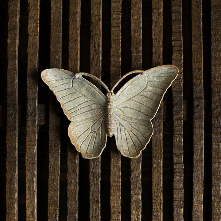 Vintage pewter butterfly trinket dish with antique zinc finish, displayed on wooden slats, captures nostalgic beauty and elegance.