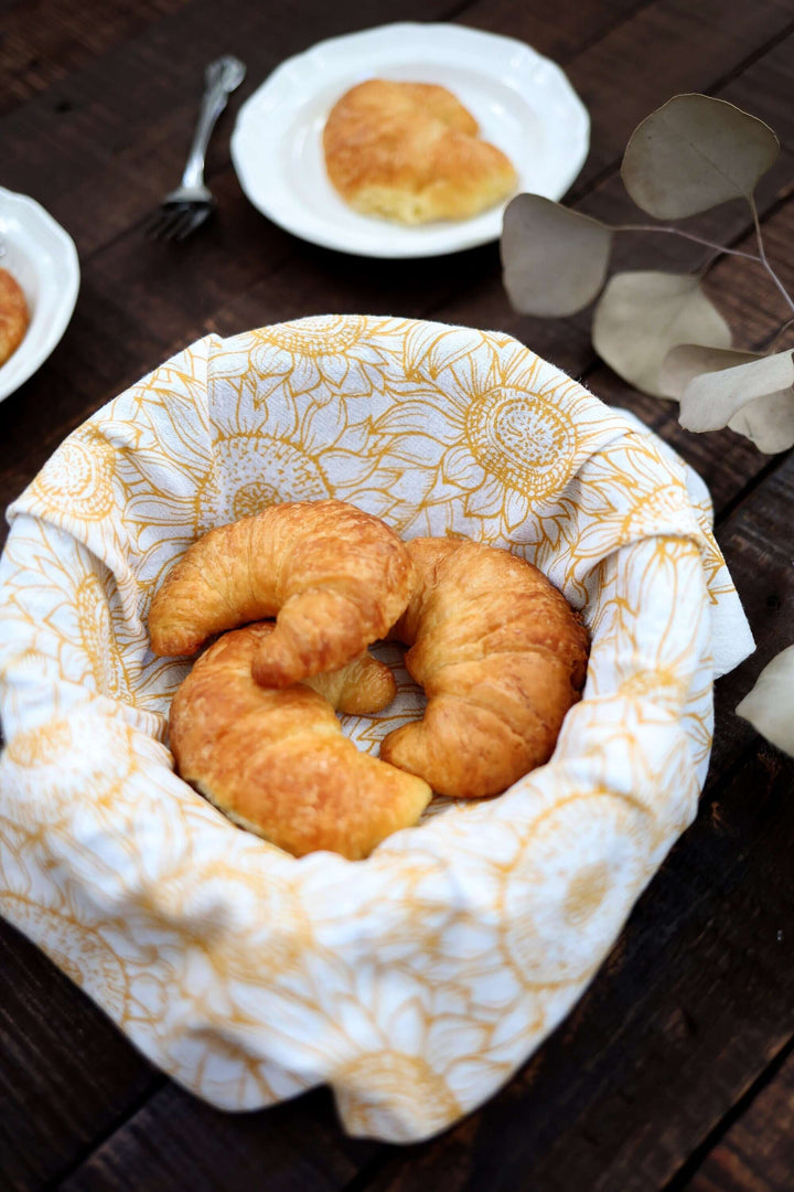 Vintage Sunflower Tea Towel lining a basket of croissants on a rustic wooden table.