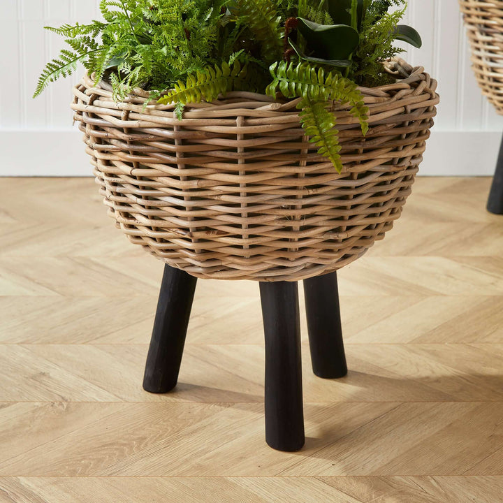 Woven rattan planter with plastic pot and wood legs, showcasing vibrant greenery and natural texture.