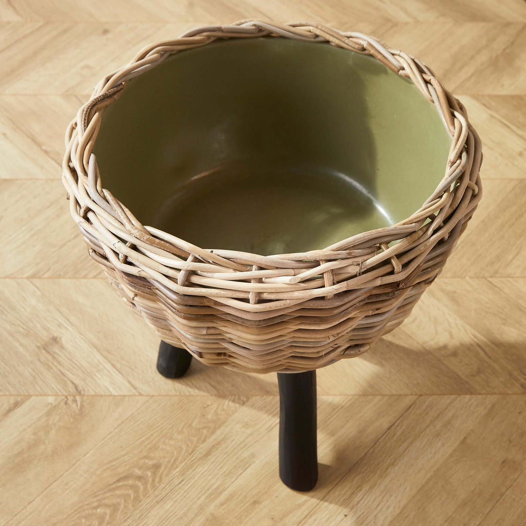 Woven rattan planter with plastic pot, featuring modern wood legs for stylish greenery display.