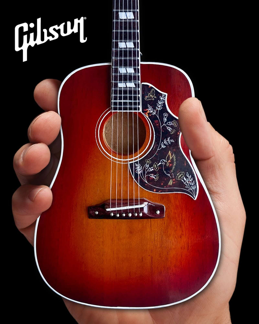 Hand holding a Gibson Hummingbird Vintage Cherry Mini Guitar Replica, showcasing intricate craftsmanship and iconic design.