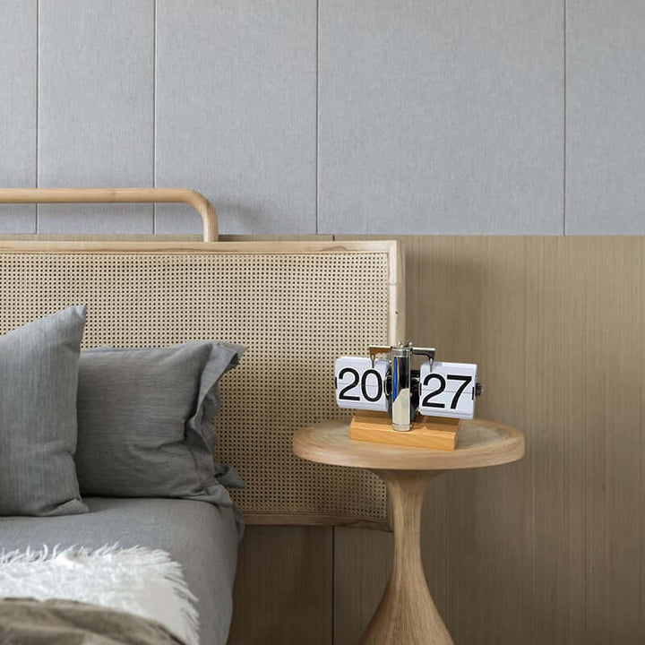 Bedroom corner with a wooden headboard, gray pillows, and a small round table with a flip clock.