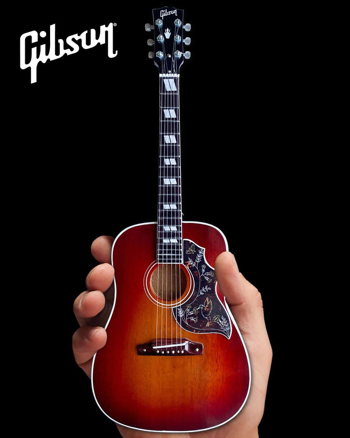 Hand holding Gibson Hummingbird Vintage Cherry Mini Guitar Replica, a 1:4 scale collectible of an iconic acoustic guitar.