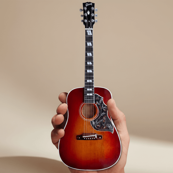 Gibson Hummingbird Vintage Cherry Mini Guitar Replica held in hand, showcasing detailed craftsmanship and iconic design elements.