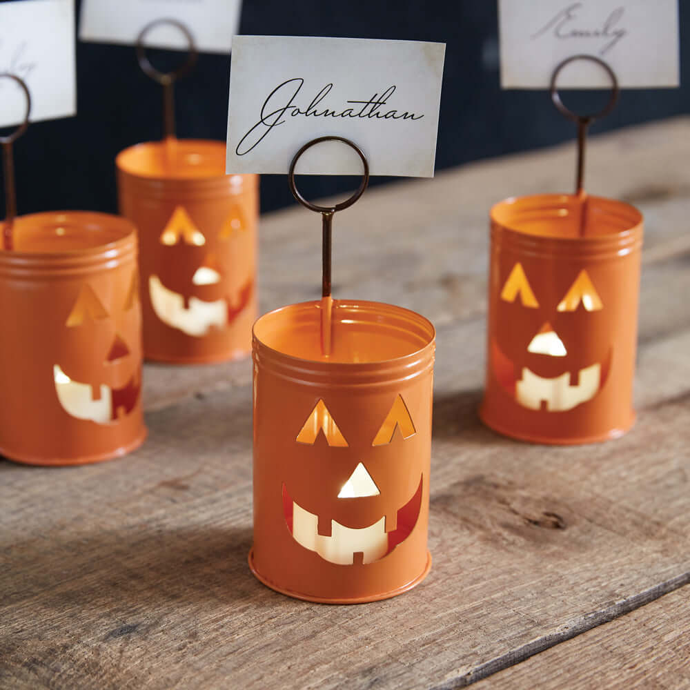 Orange metal Jack-O-Lantern place card holders on a wooden table, perfect for Halloween décor and entertaining.