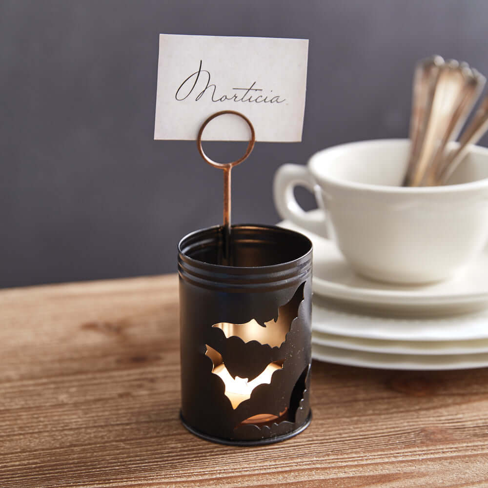 Halloween bats metal luminary place card holder on wooden table with white cups in background.