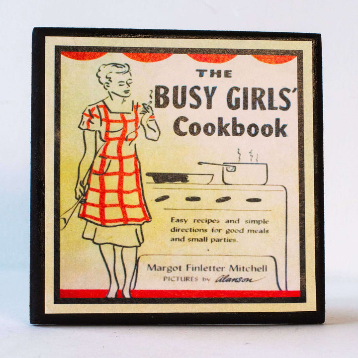 Cover of 'The Busy Girls' Cookbook' coaster with a illustration of a woman in an apron.