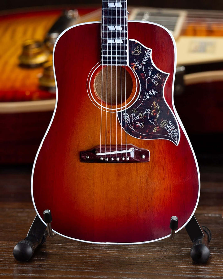 Gibson Hummingbird Vintage Cherry Mini Guitar Replica displayed on a stand, showcasing intricate design and craftsmanship.