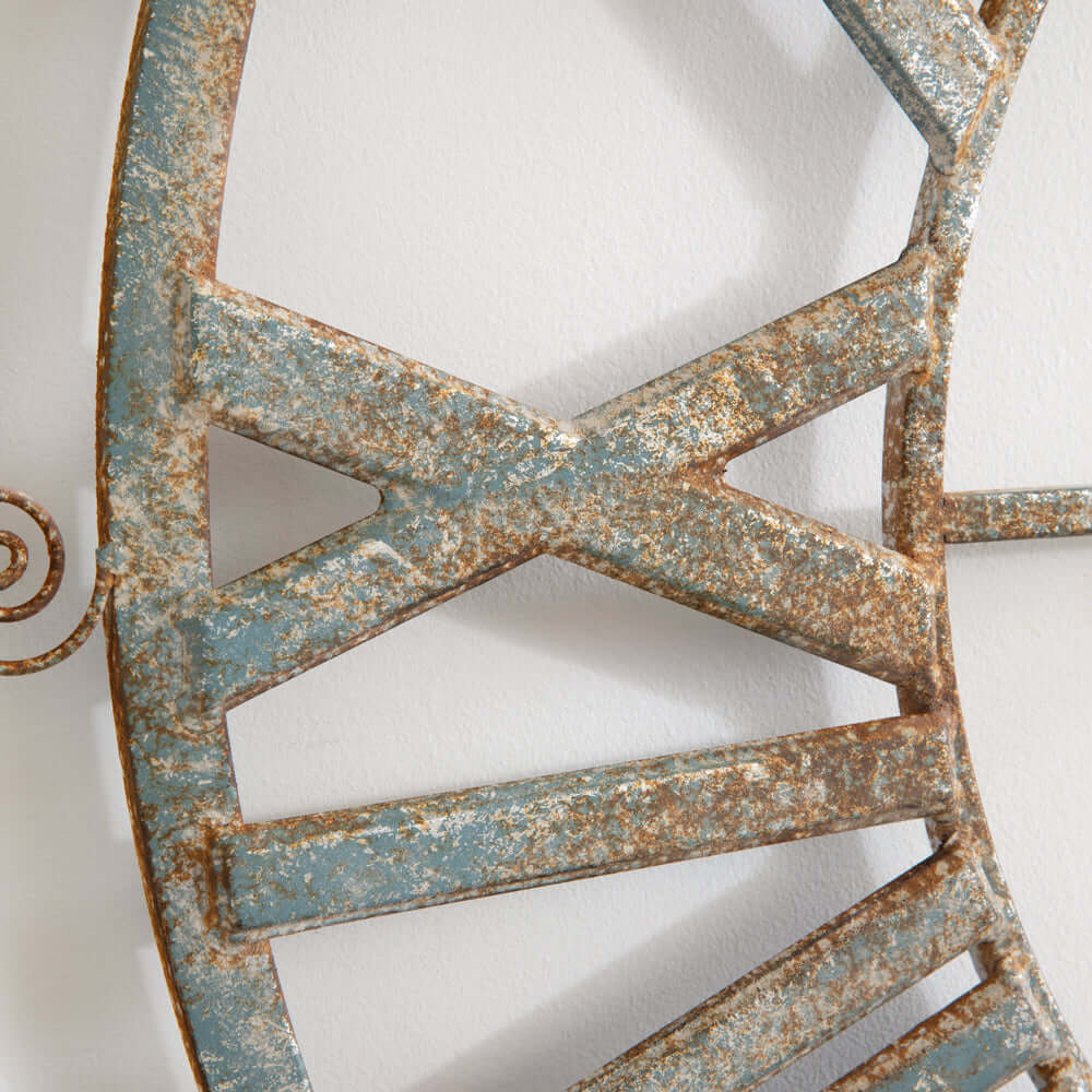 Close-up of distressed metal frame on large vintage farmhouse wall clock with Roman numerals, showcasing rustic weathered details.