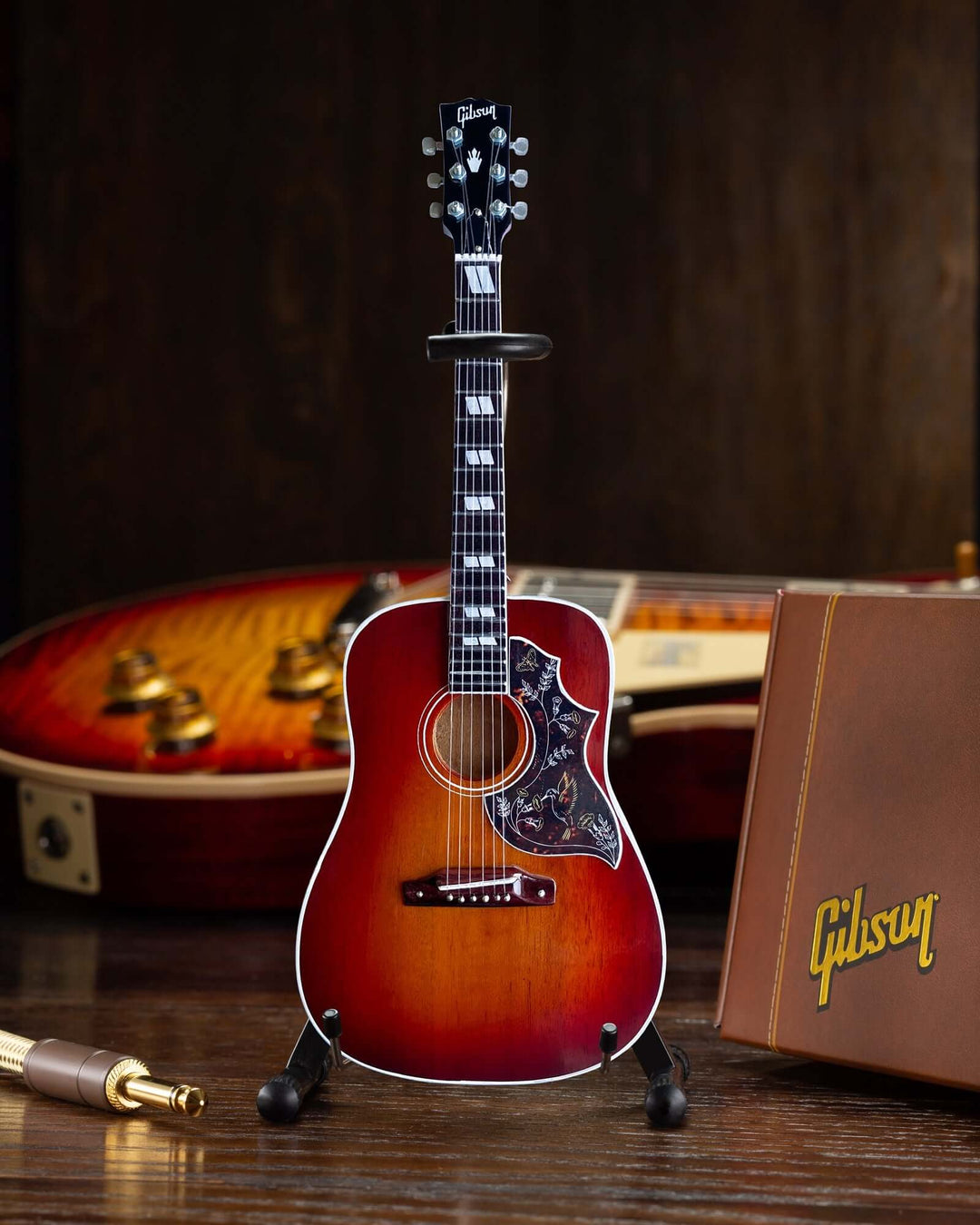 Gibson Hummingbird Vintage Cherry Mini Guitar Replica displayed with guitar case and accessories.