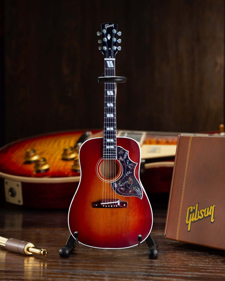 Gibson Hummingbird Vintage Cherry Mini Guitar Replica displayed with guitar case and accessories.
