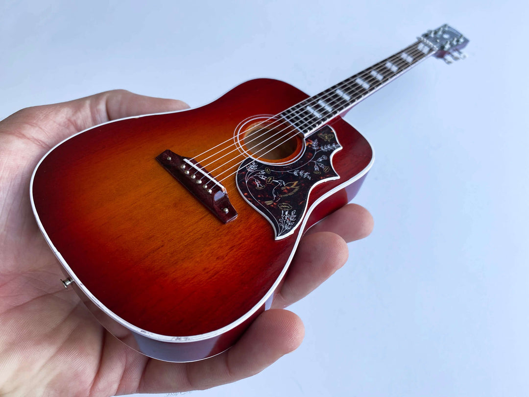 Hand holding Gibson Hummingbird Vintage Cherry Mini Guitar Replica, showcasing detailed craftsmanship of iconic acoustic guitar model.