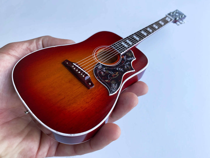 Hand holding Gibson Hummingbird Vintage Cherry Mini Guitar Replica, showcasing detailed craftsmanship of iconic acoustic guitar model.