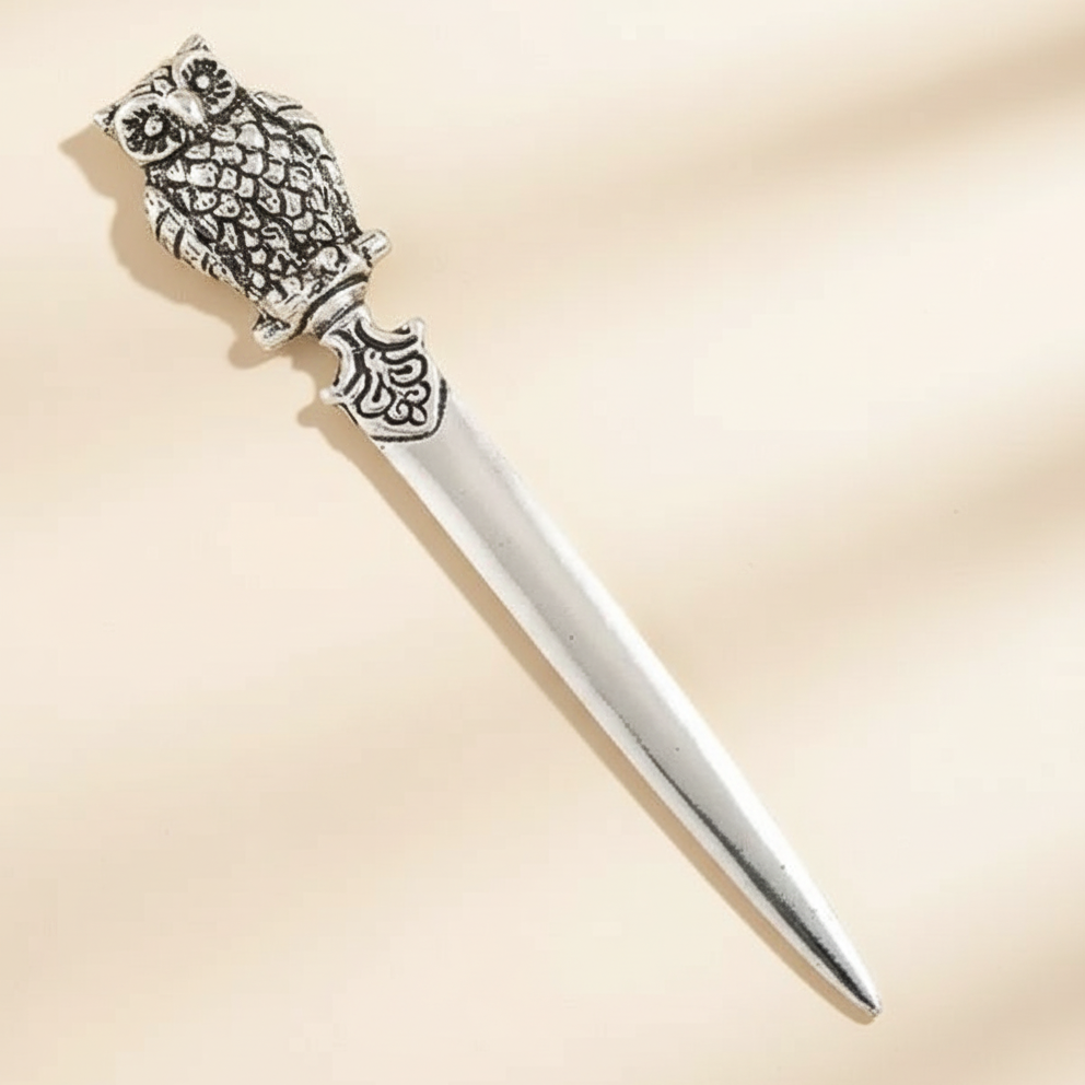 Decorative silver letter opener with intricate design on a beige background