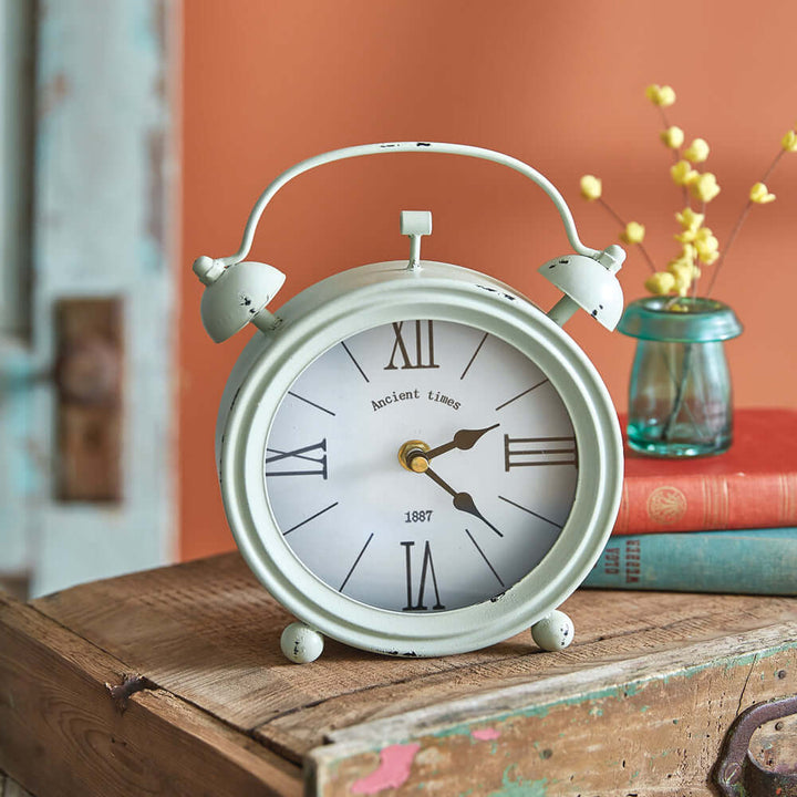Vintage mint green twin bell alarm clock with distressed edges on wooden table, evoking retro farmhouse charm in cozy setting.